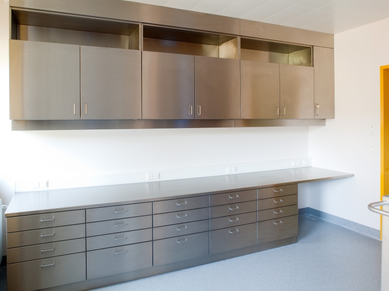 Wandverbau mit fünf Arbeitsschränken mit je vier Laden, einer durchgehend fugenlosen CNS-Abdeckung und einem CNS-Wandhängeverbau mit sieben Flügeltüren und drei offenen Fächern (komplett in Edelstahl ausgeführt)