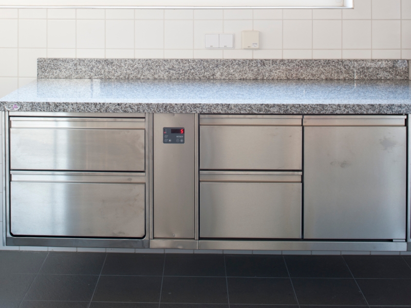 An Wand hängender Edelstahlverbau mit Hygiene-Arbeitsschränken und Granit-Abdeckung