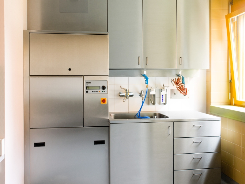 Hygiene-Verbau in Edelstahl mit extra großem Becken mit Standrohrventil, Wandhängeschrank und Unterbau mit Bügelgriffen (bündiger Wand- und Deckenanschluss mit CNS-Blenden umgesetzt)