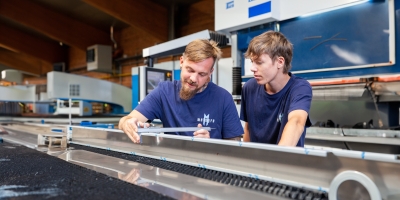Metall-Facharbeiter mit Lehrling bei der Ausbildung (Nachmessen der Blechkantung mit Messschieber)