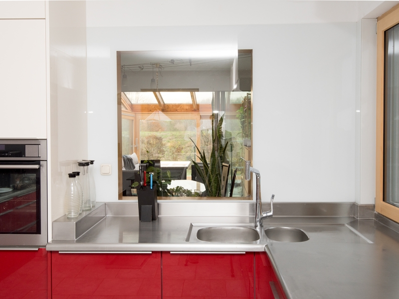 Edelstahlarbeitsplatte über Eck auf rot lackierten Holzmöbeln; Wandhochzug, Wulstrand, Doppelbecken sind fugenlos in die Edelstahlarbeitsfläche eingearbeitet