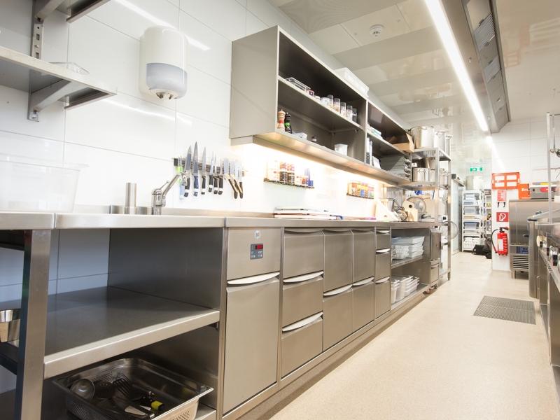CNS-Wandzeile in Großküche mit Gastronorm-Kühlung im Unterbau und offenen Wandhängeschränken mit Beleuchtung