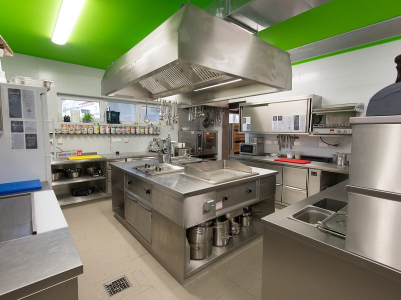 Großküche mit inidviuellem Mittelherd von Metagro (darüber hängend Dunstabzugshaube in Edelstahl)